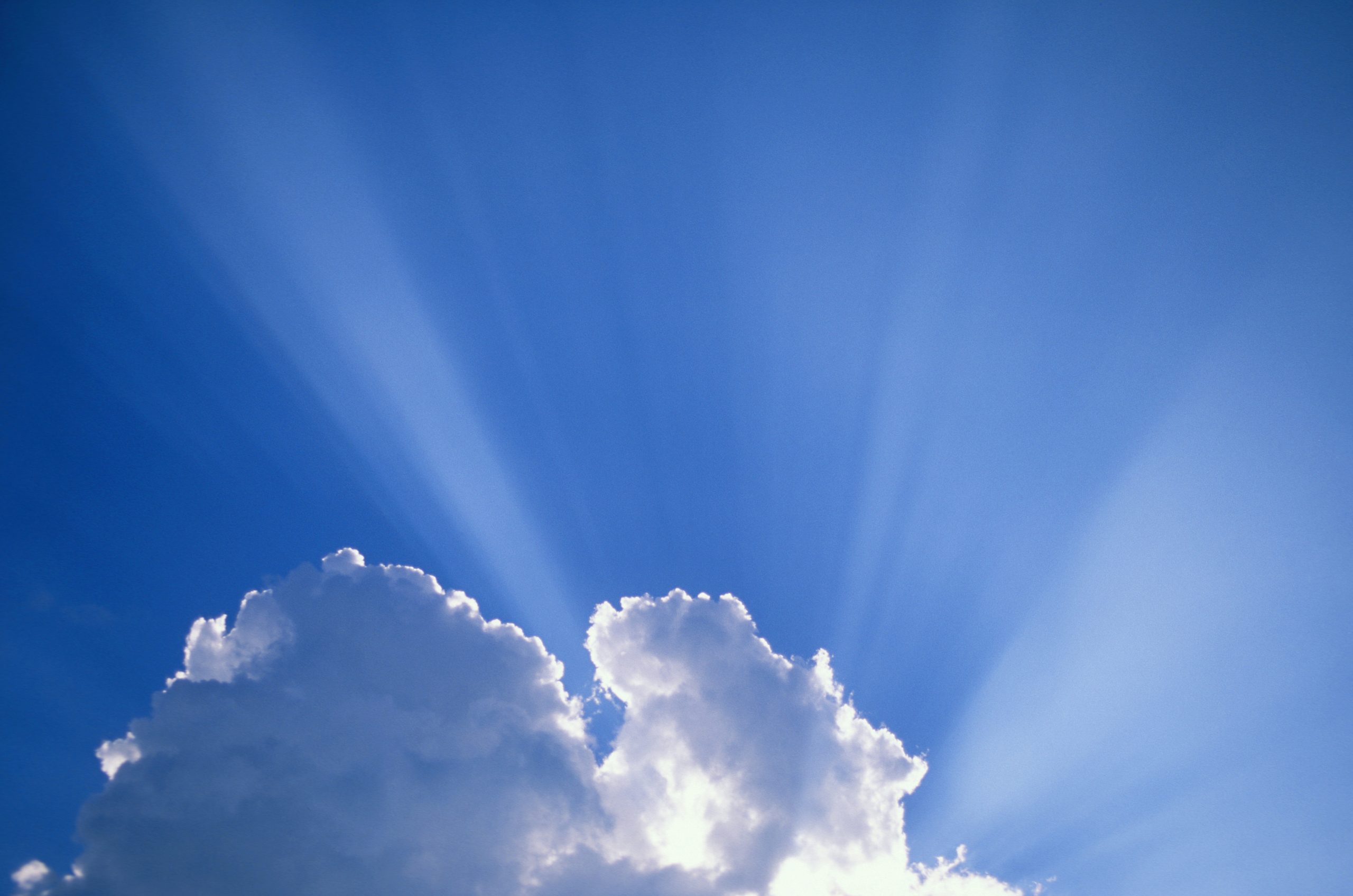 Sunrays bursting through a white cloud in the blue sky