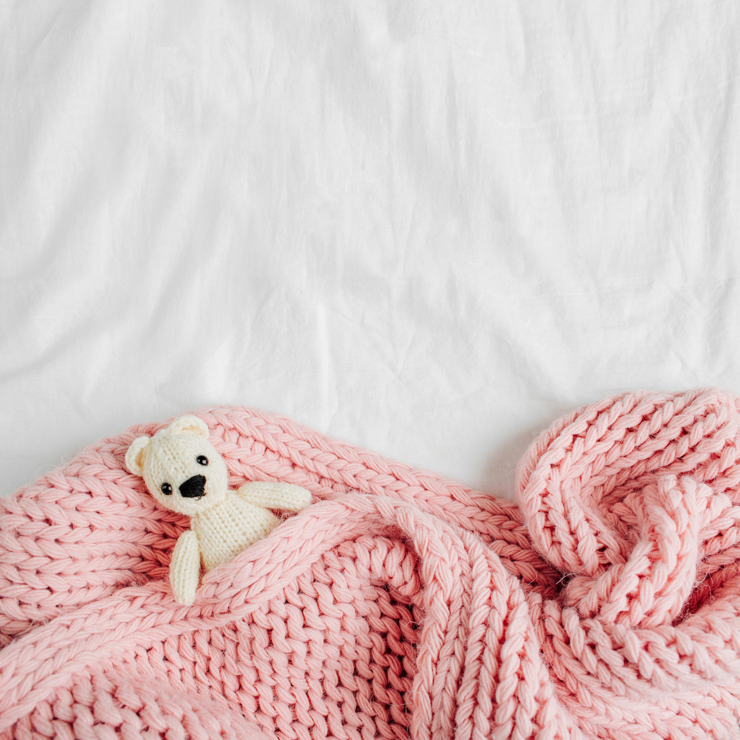 A pink baby blanket covering a small toy bear.