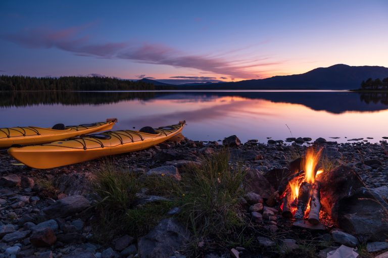 Two kayaks next to a campfire on a lake shore.